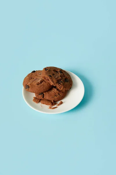 Vista de primer plano de galletas de chocolate en platillo sobre fondo azul - foto de stock