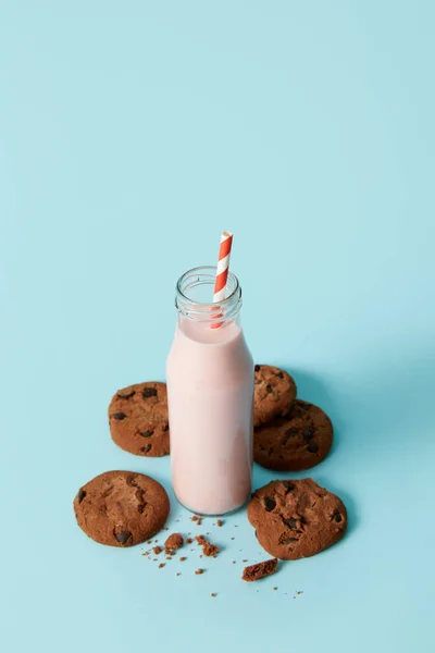 Batido de morango em garrafa com palha de bebida cercada por biscoitos de chocolate em fundo azul — Fotografia de Stock