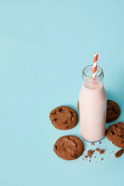 Closeup view of chocolate cookies and milkshake in bottle with drinking straw on blue background — Stock Photo