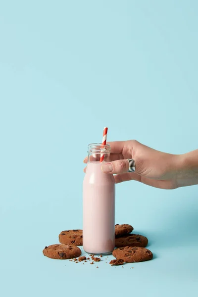 Cropped image of woman holding bottle with strawberry milkshake and chocolate cookies on blue background — Stock Photo