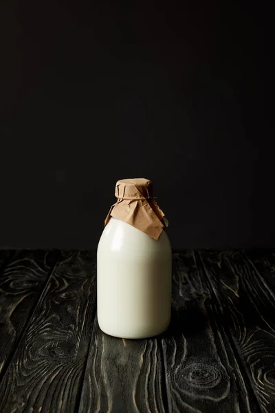 Fresh milk in bottle wrapped by paper on black background — Stock Photo