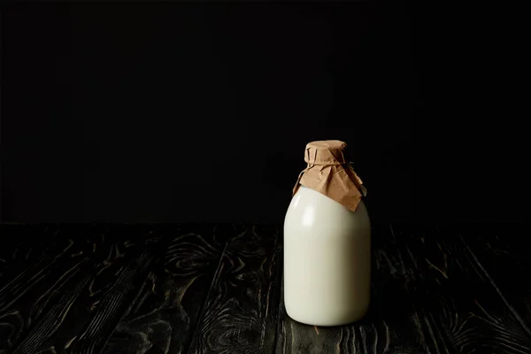 Closeup view of fresh milk in bottle wrapped by paper on black background — Stock Photo