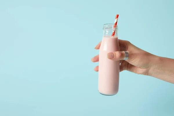 Cropped shot of woman holding strawberry milkshake in bottle with drinking straw on blue background — Stock Photo