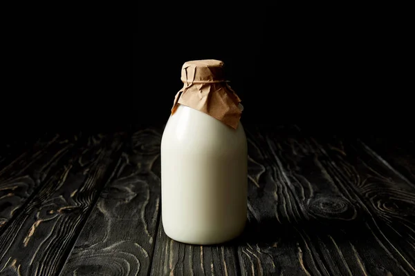 Latte fresco in bottiglia avvolto da carta su fondo nero — Foto stock