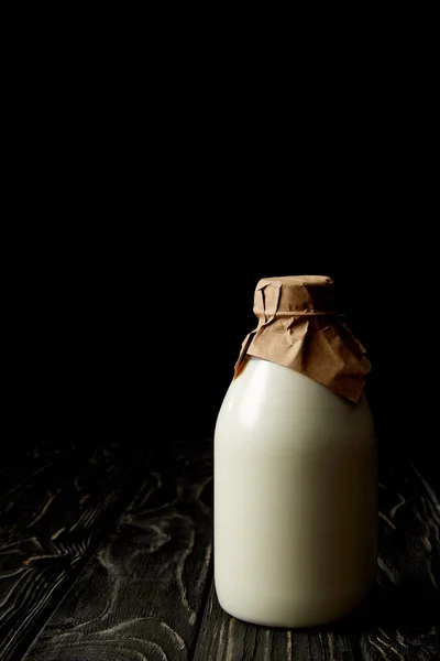 Vista de cerca de la leche fresca en botella envuelta por papel sobre fondo negro - foto de stock