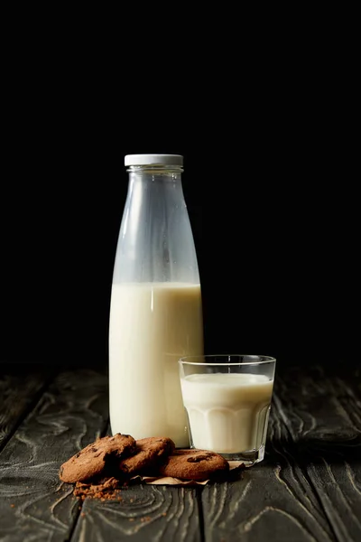 Biscoitos de chocolate, leite em garrafa e vidro sobre fundo preto — Fotografia de Stock