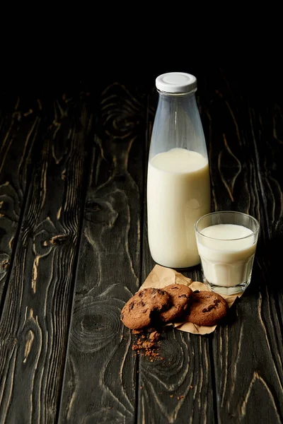 Vista close-up de biscoitos de chocolate, leite em garrafa e vidro no fundo de madeira — Fotografia de Stock