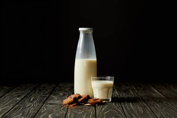 Biscotti al cioccolato, latte in bottiglia e vetro su fondo nero — Foto stock