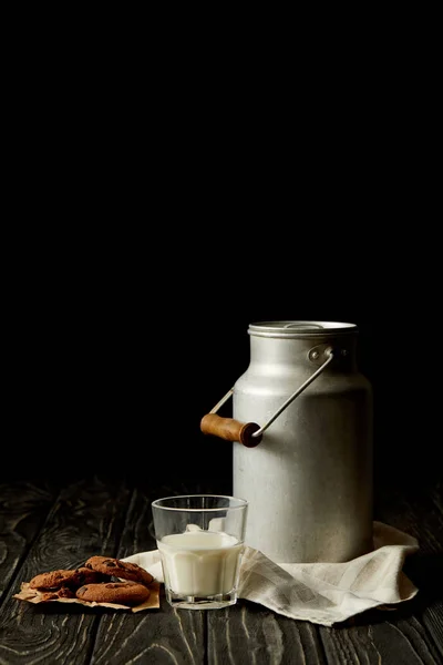 Vista de cerca de la leche en lata de vidrio y aluminio, galletas de chocolate y saco sobre fondo negro - foto de stock