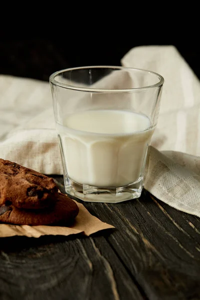 Vista close-up de vidro de leite, biscoitos de chocolate e pano de saco no fundo preto — Fotografia de Stock