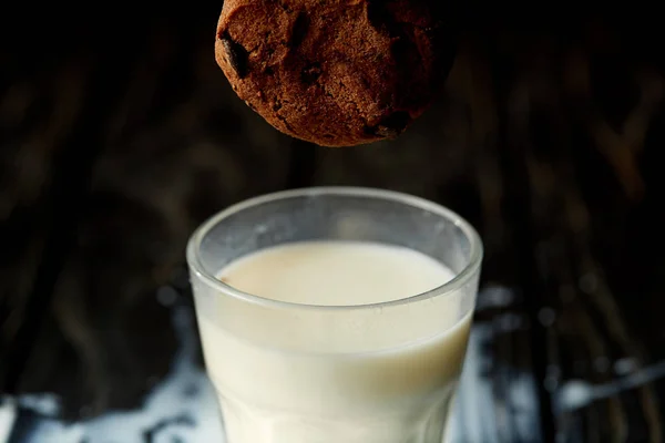 Vista de primer plano de la galleta de chocolate cayendo en un vaso con leche - foto de stock