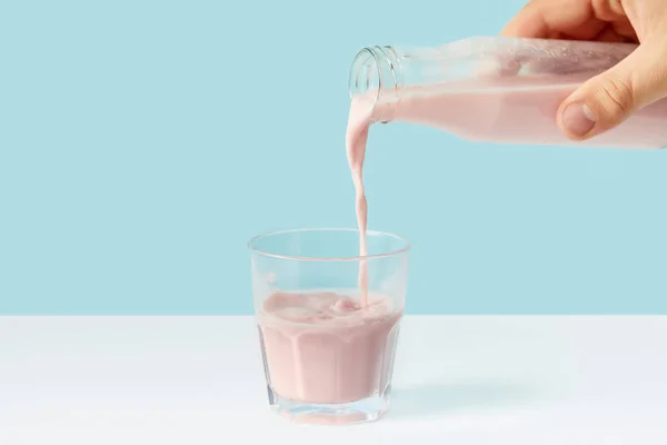 Cropped shot of man pouring strawberry milkshake into glass from bottle on blue background — Stock Photo