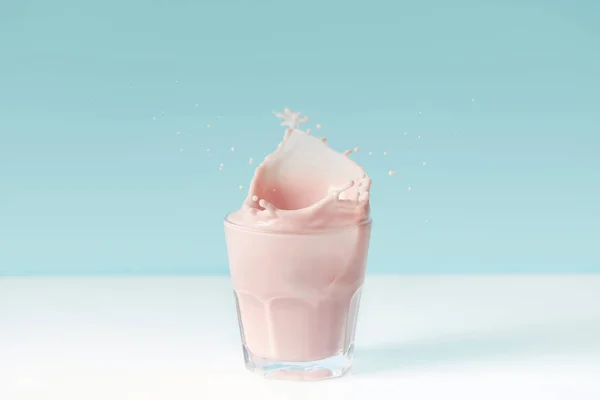 Splashing drops of strawberry milkshake from glass on blue background — Stock Photo