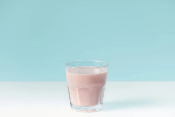 Closeup view of strawberry milkshake in glass on blue background — Stock Photo