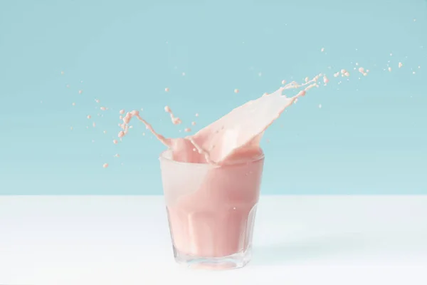 Splashing drops of strawberry milkshake from glass on blue background — Stock Photo