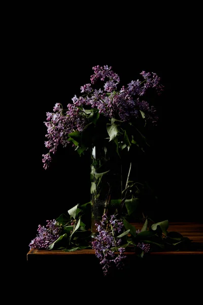 Close-up shot of branches of lilac flowers in vase isolated on black — Stock Photo