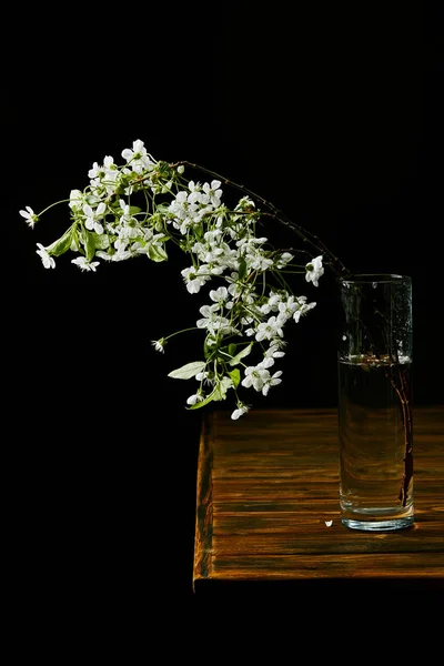 Primer plano de rama de hermosa flor de cerezo en jarrón sobre mesa de madera aislada en negro - foto de stock
