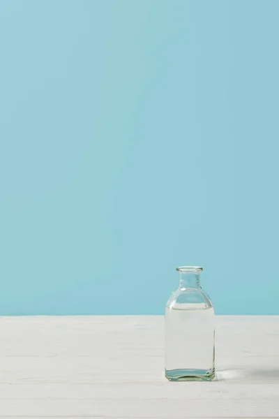 Glass bottle of water on white tabletop isolated on blue — Stock Photo