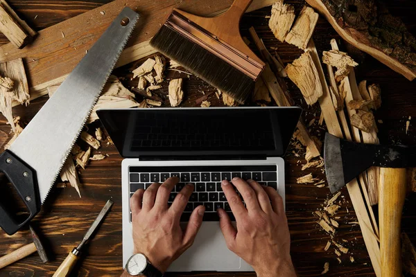 Image recadrée de charpentier tapant sur ordinateur portable entouré de différents outils sur la table — Photo de stock