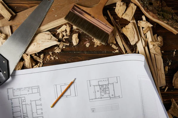 Vista superior del plano, lápiz, pincel, sierra de mano y piezas de madera sobre la mesa - foto de stock