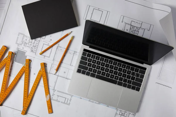 Top view of laptop with blank screen, textbook, pencils and collapsible meter on blueprint — Stock Photo