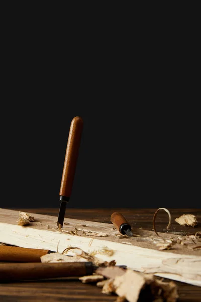 Sticking chisel in wood at table on black background — Stock Photo