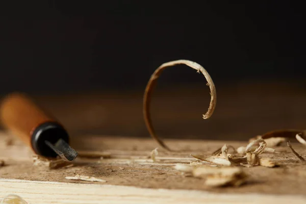 Closeup view of chisel and wooden scobs on blurred black background — Stock Photo