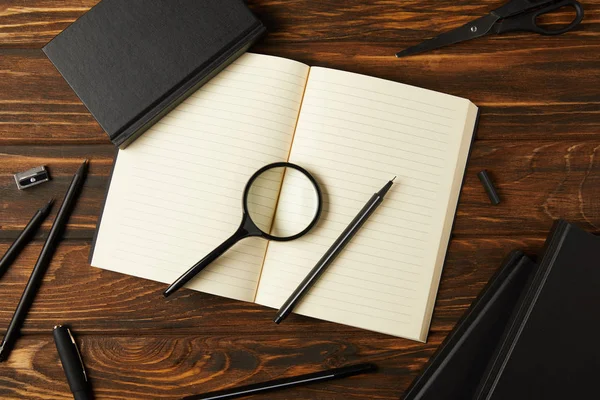 Top view of magnifying glass, notebooks and office supplies on wooden table — Stock Photo