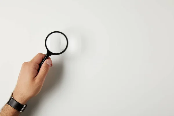 Cropped shot of male hand with wristwatch holding magnifying glass on grey — Stock Photo