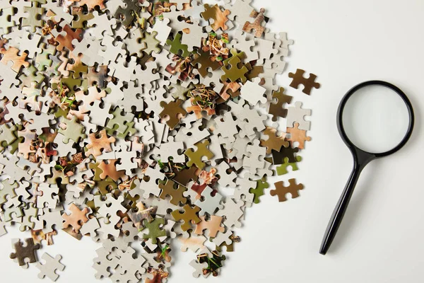 Top view of magnifying glass and jigsaw puzzle pieces on grey — Stock Photo