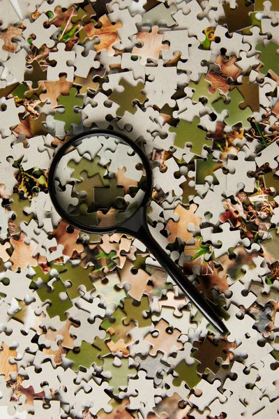 Top view of magnifying glass and jigsaw puzzle pieces on grey — Stock Photo