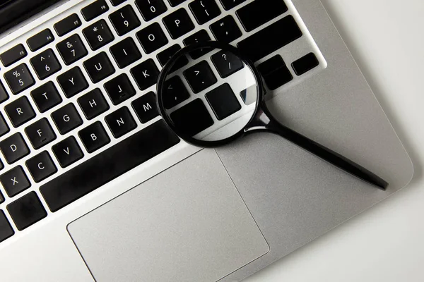 Top view of magnifying glass and laptop on grey — Stock Photo