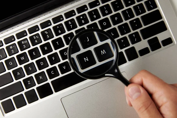 Cropped shot of person holding magnifying glass above laptop keyboard — Stock Photo