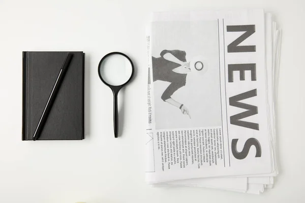 Vista dall'alto del taccuino con penna, lente d'ingrandimento e giornali isolati su grigio — Foto stock