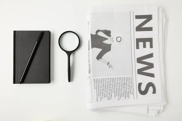 Top view of notebook with pen, magnifying glass and newspapers isolated on grey — Stock Photo