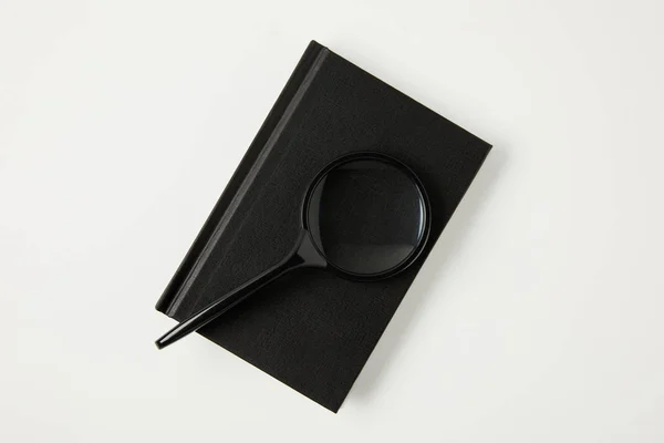Top view of magnifying glass on black notebook isolated on white — Stock Photo