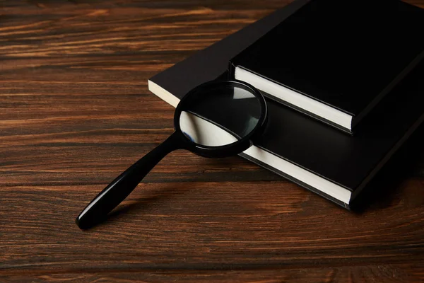 Vista close-up de lupa e livros pretos na mesa de madeira — Fotografia de Stock