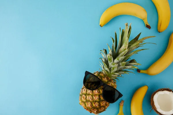 Vista dall'alto di cocco fresco, banane e ananas con occhiali da sole isolati su blu — Foto stock