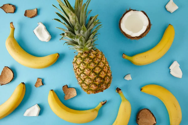 Tendido plano con piña fresca, plátanos y trozos de coco aislados en azul - foto de stock