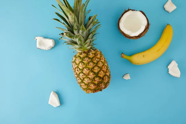 Plat avec des morceaux d'ananas mûrs, de banane et de noix de coco isolés sur bleu — Photo de stock