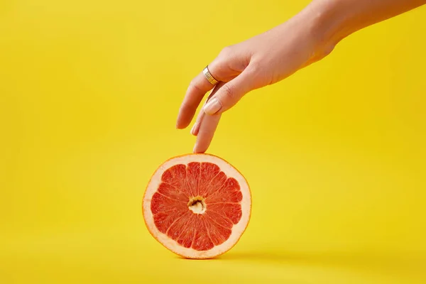 Close up view of female hand and fresh grapefruit isolated on yellow — Stock Photo