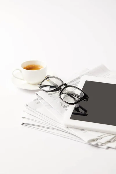 Gafas graduadas y tableta digital en la pila de periódicos y taza de café, en blanco - foto de stock