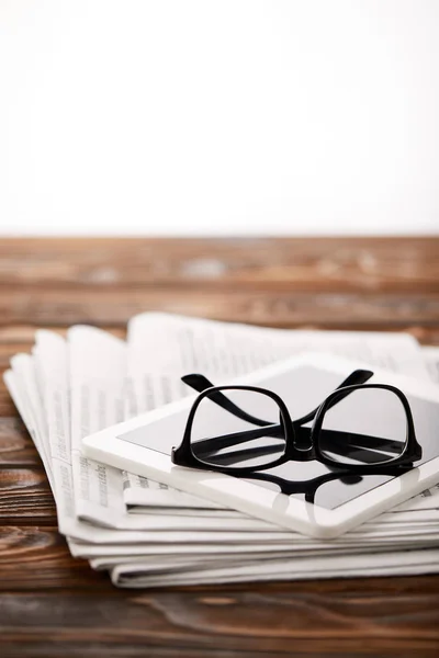 Gafas graduadas, tableta digital y pila de periódicos, sobre fondo de madera - foto de stock