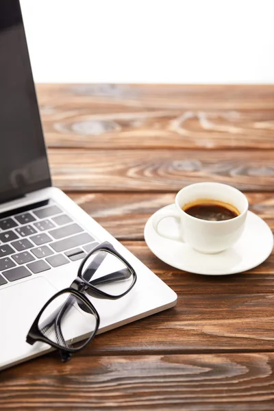 Laptop, óculos e xícara de café na superfície de madeira — Fotografia de Stock