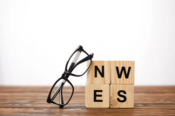 Gafas graduadas y cubos de alfabeto haciendo noticias de la palabra en la superficie de madera, sobre fondo blanco - foto de stock