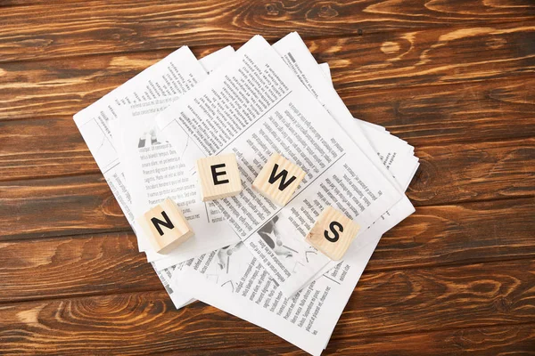 Top view of word news made of alphabet cubes on heap of newspapers on wooden background — Stock Photo