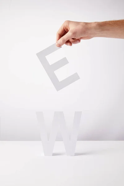 Cropped view of person holding paper letters - e and w, on white background — Stock Photo