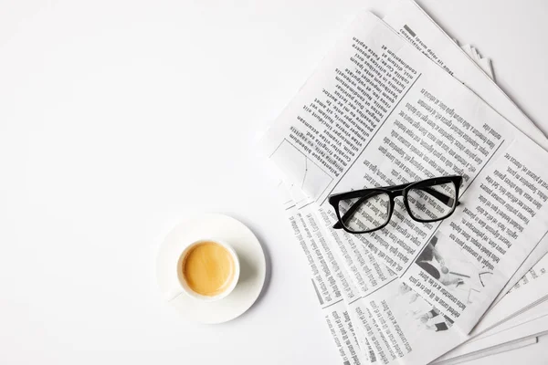 Top view of cup of coffee and eyeglasses on newspapers, on white table — Stock Photo