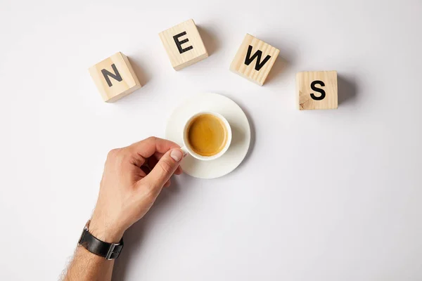 Vista parziale di persona con tazza di caffè e parola parola notizie parola fatta di blocchi di alfabeto in legno, su sfondo bianco — Foto stock