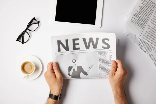 Cropped view of businessman reading newspaper at white table with digital tablet, coffee and eyeglasses — Stock Photo